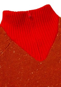 Close-up van een geribbelde rode kraag met een kwart rits op een gespikkelde bruine gebreide trui.