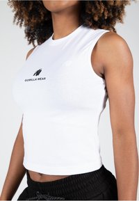 Witte mouwloze crop top van katoen met een getailleerd ontwerp, met een zwart 'Gorilla Wear' logo in het midden en een soepele textuur.