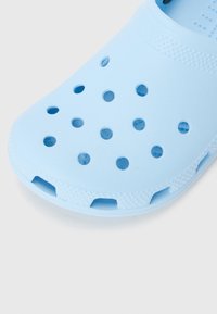 Light blue rubber clog featuring multiple ventilation holes and textured surfaces. Open-back design with a slightly raised heel and flexible material.
