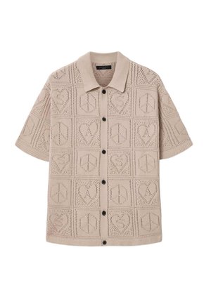 Beżowy krótki sweter kardigan z krótkim rękawem i czarnymi guzikami, z wzorem serc i znaków pokoju ułożonych w kratkę.