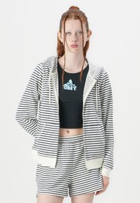 Pull à rayures en marine et blanc avec fermeture éclair, associé à un crop top noir avec un logo et un short rayé. Texture de tissu lisse.