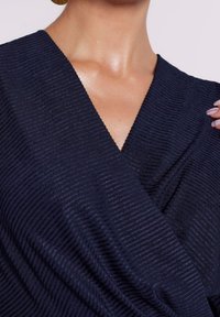 Haut cache-cœur texturé bleu marine avec rayures verticales, col en V, et tissu doux, mettant l'accent sur des éléments polyvalents et élégants.