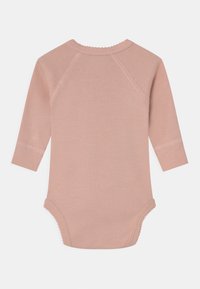 Hosszú ujjú bodysuit, puha rózsaszín pamutból készült, kerek nyakkivágással, fodros díszítéssel és patentos záródással az alján.