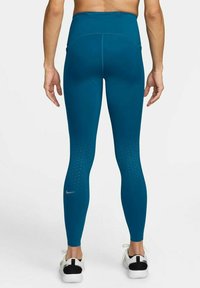 Teal legging korkealla vyötäröllä, joissa on sileä pinta, ja jotka sisältävät rei'itettyjä kuvioita nilkoissa sekä pienen hopeisen logon takana.