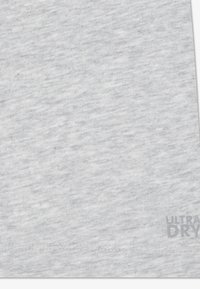 Ανοιχτό γκρι ύφασμα με διακριτή ελαφρώς αραιωμένη υφή, που φέρει τυπωμένη ετικέτα «ULTRA DRY» σε ανοιχτό γκρι χρώμα στην κάτω δεξιά γωνία.