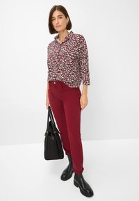 Chemise multicolore avec un col, motif abstrait noir et blanc, associée à un pantalon bordeaux et des bottines noires. Sac à main noir inclus.