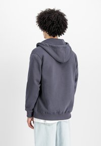 Μπλε φόρμα με κουκούλα και κορδόνι, με ribbed μανσέτες, φτιαγμένη από μαλακό ύφασμα. Φοριέται πάνω από ένα άσπρο πουκάμισο και ανοιχτό μπλε τζιν. Απλός, καθημερινός σχεδιασμός.