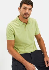 Lichtgroen polo shirt met een klassieke kraag, korte mouwen en een subtiele logodetail. De stof lijkt glad en heeft een katoenmix textuur.