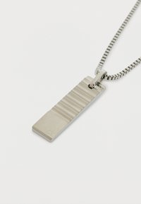 Collar de metal con un colgante rectangular que presenta surcos texturizados, suspendido de una cadena elegante con un patrón. Logo grabado presente.
