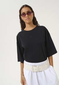 Sort oversized t-shirt med korte ærmer og subtile broderede logo, parret med et bredt hvidt bælte og løse hvide shorts.