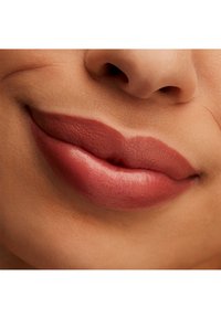 Matowa pomadka w ciepłym odcieniu mauve podkreśla pełne usta, ukazując gładką teksturę i wyraźne krawędzie bez połysku. Odcień skóry jest naturalny.
