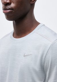 Close-up of a person wearing a light gray Nike shirt with a small gray Nike swoosh logo on the chest, neutral background.