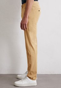 Lichtbeige katoenen broek met een recht gesneden ontwerp, voorzien van een enkele achterzak en een gladde textuur. Combinatie met witte sneakers.