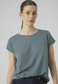 Teal kortom mouwtop gemaakt van zachte stof met een ontspannen fit. Heeft een ronde halslijn en opgerolde mouwen, gecombineerd met donkere jeans.
