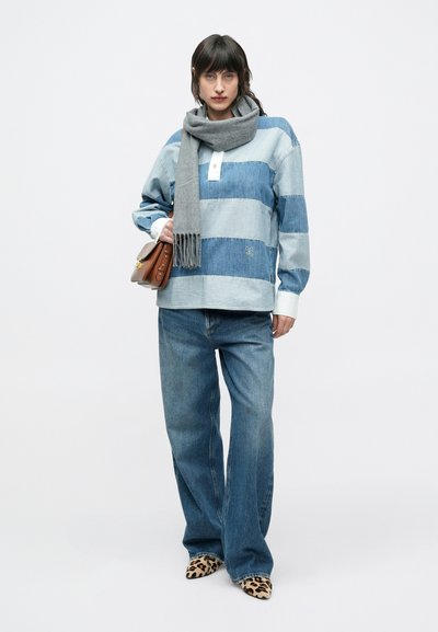 Chemise en denim oversize à rayures horizontales bleues, patte de boutonnage blanche, associée à un jean large et des chaussures à imprimé léopard. Accessoire écharpe grise.