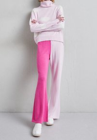 Hellrosa Rollkragenpullover mit Wolkenmuster, kombiniert mit weit geschnittenen Hosen in einem Farbverlauf von Pink. Weiße Clogs runden das Outfit ab.