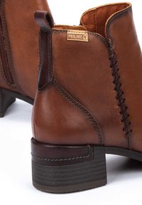 Braune Leder-Ankle-Boots mit einem seitlichen Reißverschluss, dekorativer Naht und einem Blockabsatz. Pikolinos-Logo an der Seite.