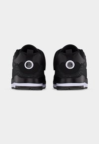 Ζευγάρι μαύρα αθλητικά παπούτσια με λευκές ενδιάμεσες σόλες, υφασμάτινες λεπτομέρειες, κυκλικά λογότυπα στους τακούνες και θηλιές σε ανοιχτό φόντο.