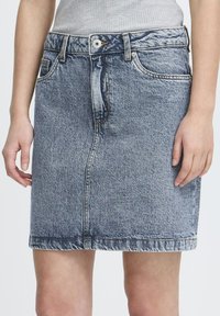 Jupe en denim bleu clair, de longueur mi-cuisse, avec des détails de couture visibles, des poches et une fermeture à bouton en métal à la taille.