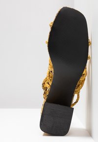 Żółta, pleciona sandały z teksturowaną cholewką i czarną gumową podeszwą. Posiada otwarty krój oraz niski, blokowy obcas.