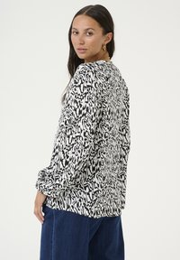 Blouse à manches longues avec un motif abstrait noir et blanc, offrant une coupe décontractée, un matériau léger et un col rond.