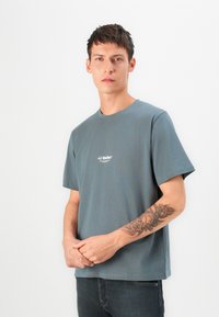 Tricou din bumbac gri, cu mâneci scurte și decolteu rotund. Prezintă un mic logo alb pe piept. Croială lejeră.