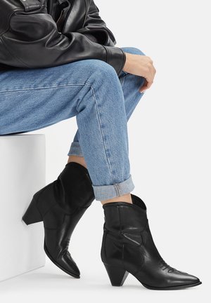 Černé kožené kovbojské boty s špičatou špičkou a volným svrškem. Disponují nízkým podpatkem a jemnými švy.
