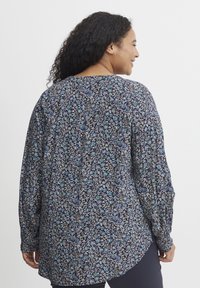 Blúzka s dlhým rukávom v námorníckej modrej farbe s kvetinovým vzorom, s okrúhlym výstrihom, voľným strihom a elastickými manžetami. Materiál vyzerá ľahký a textúrovaný.