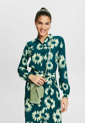 Teal kjole med blomsterprint, knaplukning, lange ærmer og bælte i taljen. Begyndt med en lille grøn crossbody taske.
