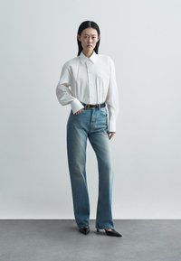 Λευκό πουκάμισο με χαλαρή εφαρμογή και μία τσέπη στο στήθος, συνδυασμένο με ξεθωριασμένα μπλε τζιν ίσιας γραμμής, μαύρη ζώνη και μυτερές μαύρες γόβες.