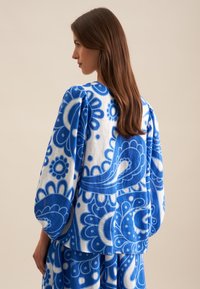 Blusa blu e bianca con ampi motivi paisley e floreali, dotata di maniche a palloncino e una vestibilità morbida. Presenta una superficie liscia.