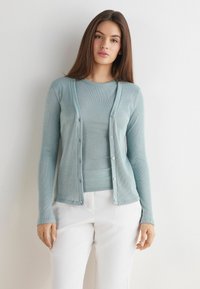 Jasnoniebieski kardigan wykonany z miękkiego, lekko prążkowanego materiału, z zapięciem na guziki z przodu i długimi rękawami, w zestawie z pasującym topem.
