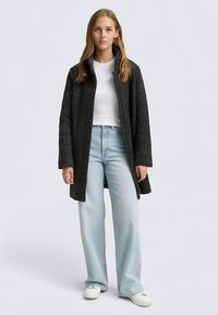 Cappotto in misto lana grigio scuro con colletto alto, tasche laterali e maniche lunghe, indossato sopra una maglietta bianca e jeans a gamba larga color azzurro chiaro.