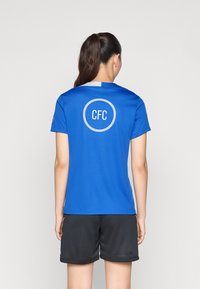 Sininen lyhythihainen urheilu-paita, jossa on pyöreä "CFC" -logo selässä, yhdistettynä mustiin shortseihin. Kangas on kevyt ja teksturoitu.