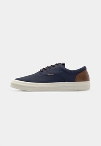 Navy canvas sneaker with brown leather accents, white rubber sole, round toe, and brown laces. Simple, low-profile design.