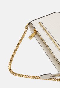 Witte handtas van getextureerd leer met een gouden schakelkast, ritssluiting en contrasterende donkere biezen.
