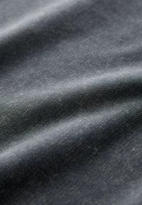 Țesătură de denim închis, cu o textură netedă, având variații subtile de nuanță și un ușor luciu, evidențiind cutele și pliurile.