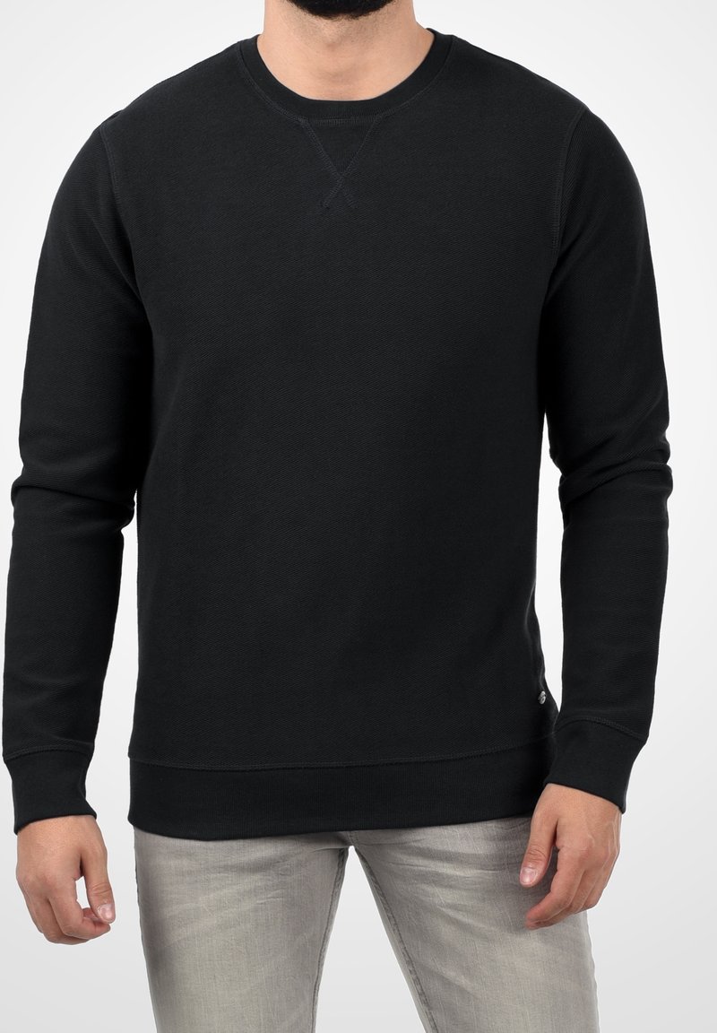 Czarna bluza crewneck z długimi rękawami, ściągaczami przy mankietach i dole, miękka w dotyku, z małym logo umieszczonym w pobliżu dolnego brzegu.