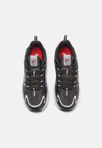 Scarpe da ginnastica nere con tomaia in rete, presentano accenti bianchi, una suola spessa e lacci. Logo Fila visibile sulla linguetta e sui lati superiori.