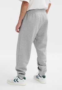 Grijze sweatpants met een elastische tailleband en boorden, voorzien van zijzakken. Gepaard met witte sneakers met groene en blauwe strepen.