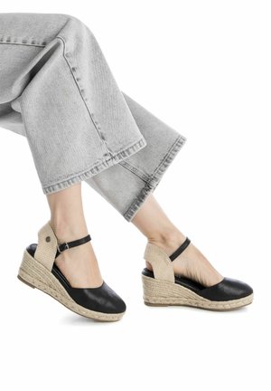 Sandalias de cuña negras con suela de yute trenzado, parte superior de cuero suave y una correa texturizada beige alrededor del tobillo. Diseño casual con talón abierto.