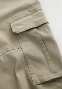 Khaki stof cargo-lompe med klap og synlige søm på casual bukser, vist i nærbillede.