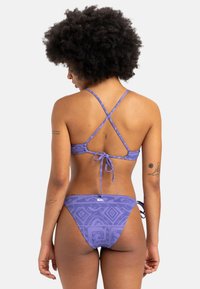 Lila Bikini-Set mit strukturiertem Muster, Spaghetti-Trägern und einer Band-Verschluss hinten. Die Unterteile haben ein ähnliches Design mit einem niedrigen Bund.
