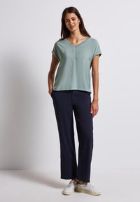 Top verde menta a maniche corte con scollo a V. Abbinato a pantaloni larghi blu navy e sneakers bianche. Tessuto morbido con una leggera lucentezza.