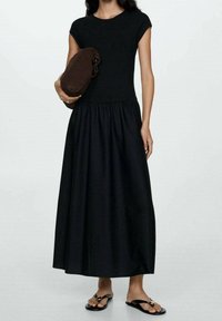 Robe maxi noire avec un corsage ajusté et une jupe évasée. Fabriquée en tissu doux, elle présente des manches courtes et est accompagnée d'une pochette marron.