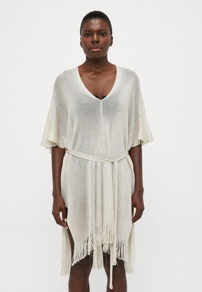 Copertura in pizzo color beige chiaro con vestibilità morbida, scollatura a V e maniche corte. Presenta una cintura da annodare e un orlo frangiato per un tocco di dettaglio in più.