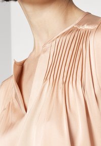 Blouse pêche brillante avec de fines plissures verticales sur l'épaule et un décolleté en V sur la partie supérieure de la poitrine et du cou d'une personne.