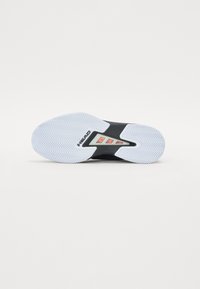 Semelle de chaussure de sport noire avec un motif en zigzag blanc, présentant une surface texturée et une découpe centrale avec un logo en contraste.