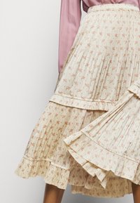 Falda midi floral plisada con una base crema y pequeñas flores rosas, volantes en capas y un diseño de rayas texturizadas.