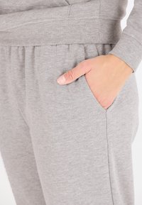 Grau gestalteter Hoodie aus weichem Stoff, mit gerippten Bündchen und einer Seitentasche auf der linken Seite, sowie dezentem Branding am Saum.